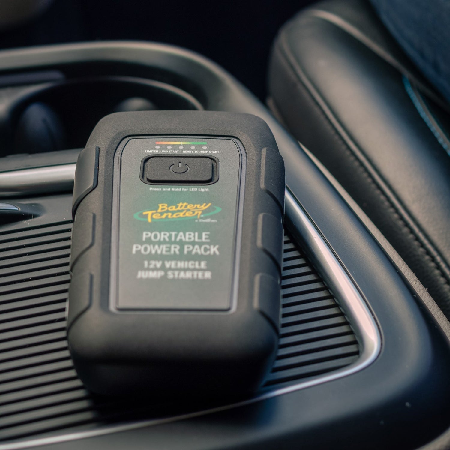 A portable jump starter and power bank sits on a middle console in a car.